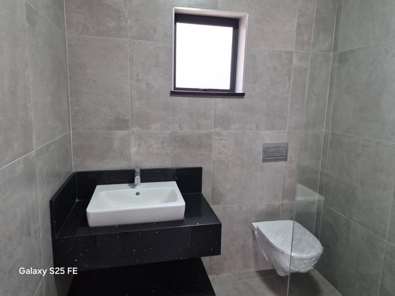 Modern bathroom featuring grey wall tiles, a floating vanity with a black countertop, and a wall-mounted toilet with a concealed cistern.