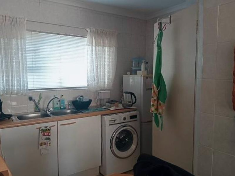 A functional kitchen area featuring tiled walls, laminate countertops, a double sink, and an integrated washing machine space.