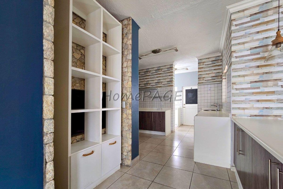 A kitchen area featuring built-in shelving, stone-clad accents, tiled flooring, and modern cabinetry with a neutral backsplash.