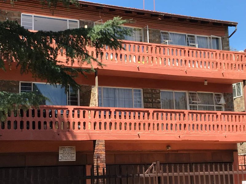 Exterior view of a multi-story apartment building featuring balconies with decorative railings, stone cladding, and metal security fencing at the ground level.