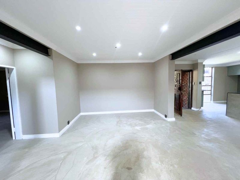 A spacious, open-plan living area featuring polished concrete floors, exposed steel beams, and modern recessed downlighting, offering a clean, neutral canvas for interior design.