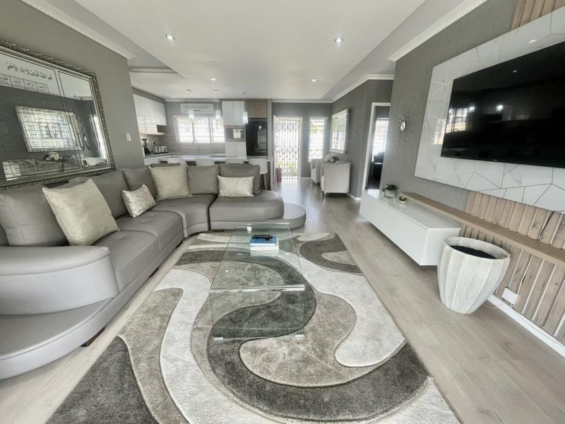 Modern open-plan living area featuring laminate flooring, recessed lighting, and a sleek built-in media wall, seamlessly flowing into a contemporary kitchen space.