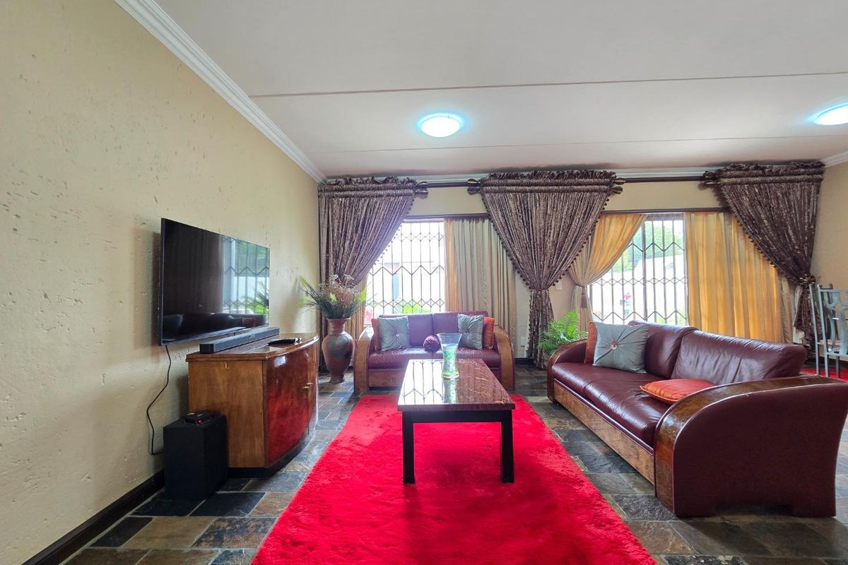 A spacious living room featuring natural stone flooring, decorative ceiling cornices, and security bars on the windows.