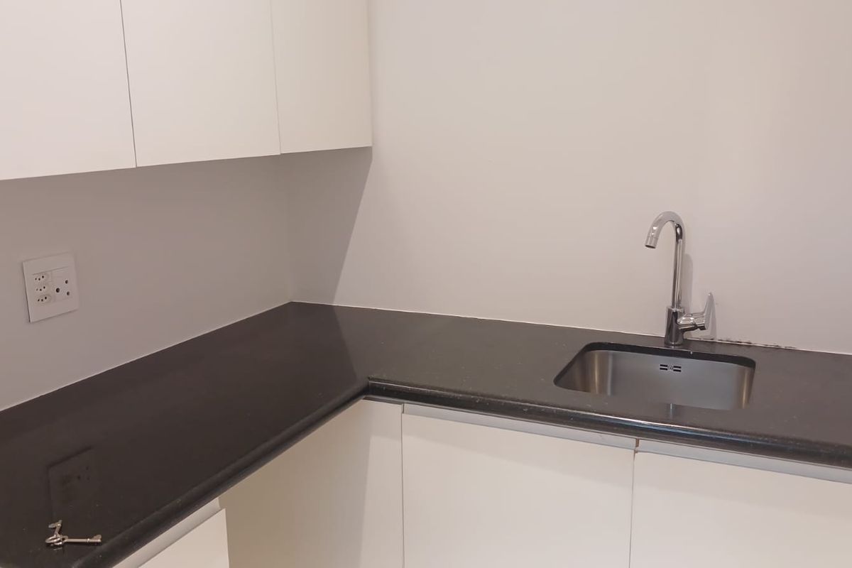 A clean, modern kitchenette featuring white cabinetry, dark stone countertops, and a stainless steel sink with a chrome faucet.
