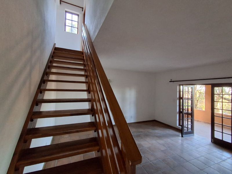 Open-plan living area featuring a wooden staircase, tiled flooring, and french doors leading to an outdoor space.