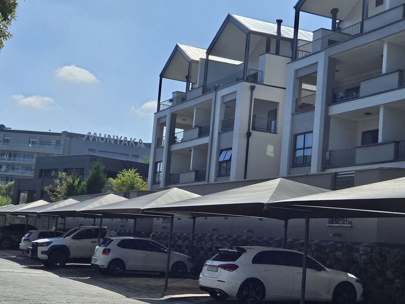 Exterior view of a modern apartment complex featuring covered parking bays, paved driveway, and private balconies on each level.
