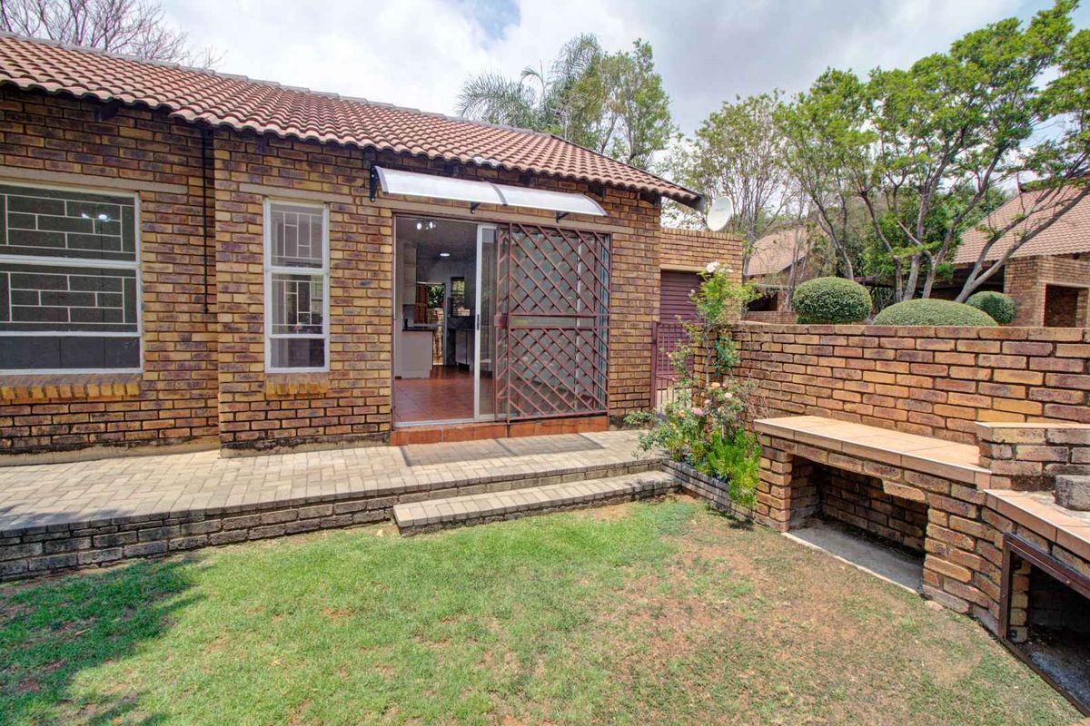 Rear view of the townhouse featuring a paved patio area, built-in brick braai, and a small private garden with access to the interior.