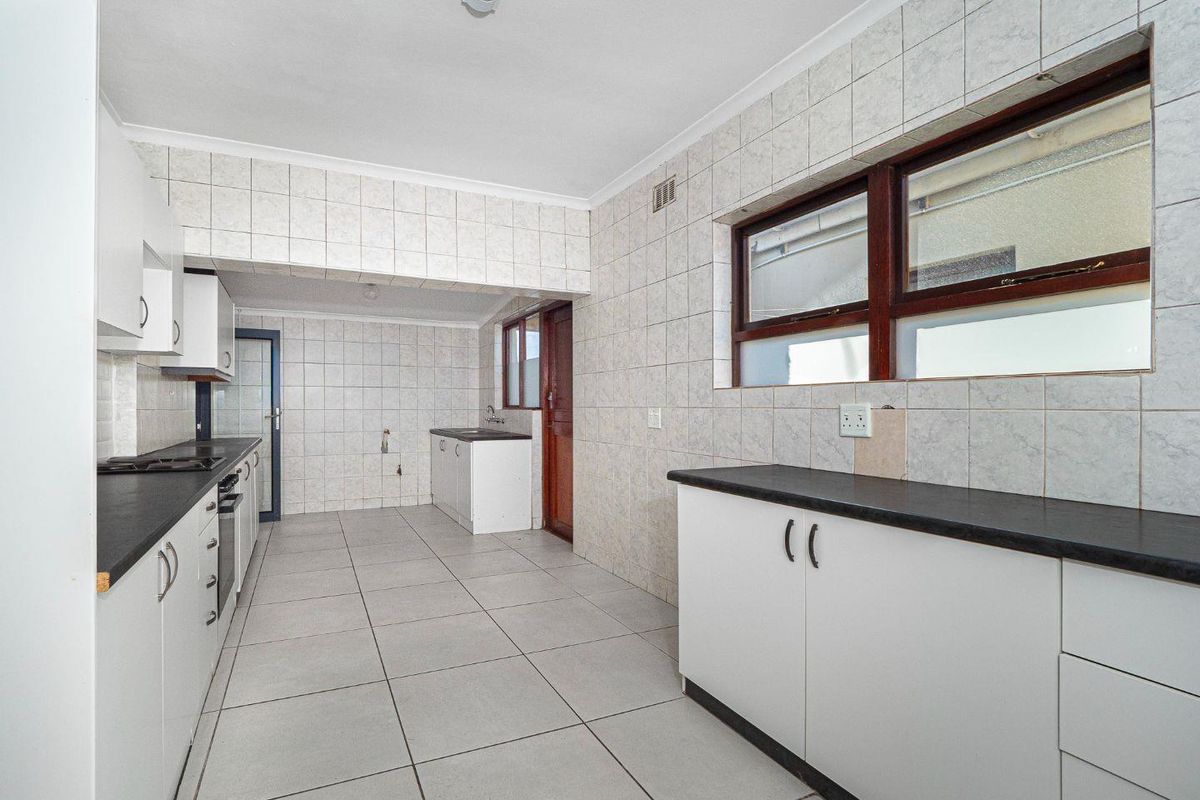 A spacious, empty kitchen featuring white cabinetry, dark laminate countertops, and full-height ceramic wall tiling, offering a functional layout ready for modernization.