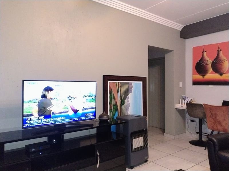 A living room area featuring tiled flooring and decorative ceiling cornicing, with a functional layout and a built-in wall niche.
