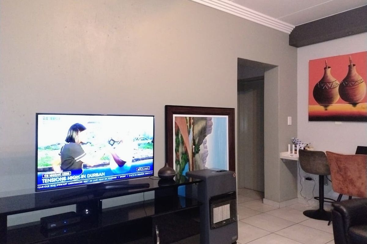 A living room area featuring tiled flooring and decorative ceiling cornicing, with a functional layout and a built-in wall niche.