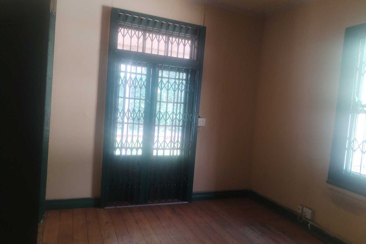 An empty room featuring original timber flooring, security gates on the door, and large windows allowing natural light.