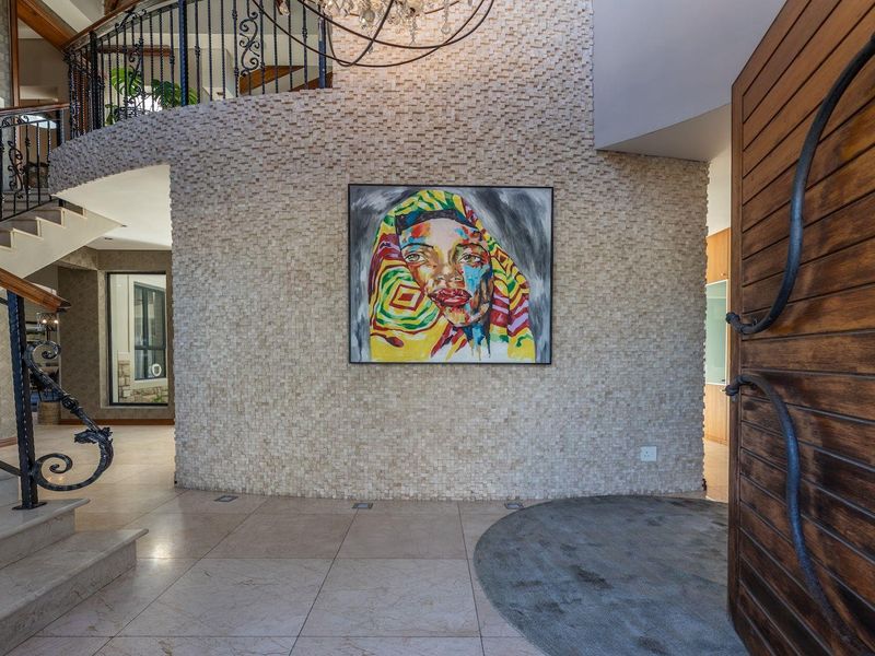 Grand entrance hall featuring a striking stone mosaic feature wall, elegant curved staircase with wrought iron balustrade, and polished stone flooring.