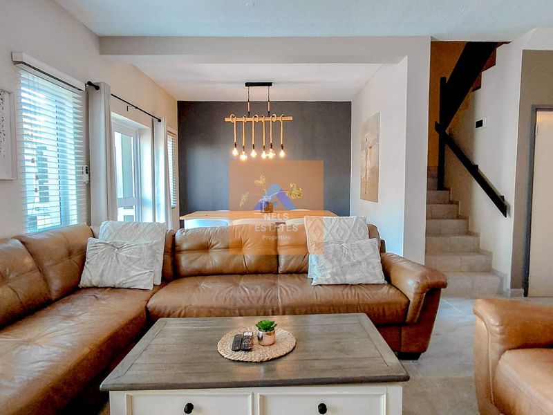 Open-plan living and dining area featuring tiled flooring, modern pendant lighting, and a staircase leading to the upper level.