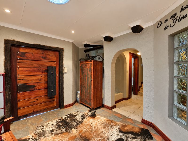 Welcoming entrance hall featuring a rustic solid wood front door, arched architectural details, glass block window, and durable tiled flooring with exposed timber ceiling beams.