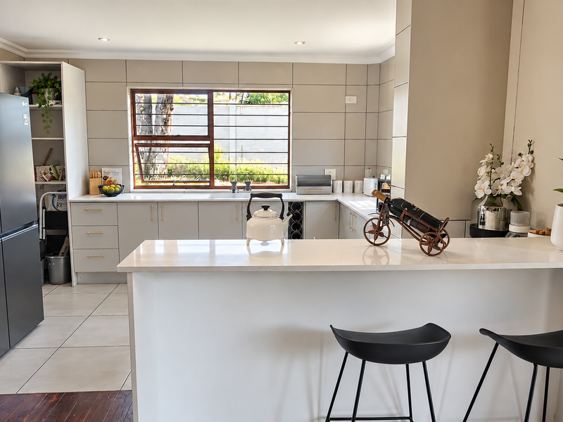 Modern kitchen featuring sleek cabinetry, stone countertops, a breakfast bar, and a tiled splashback with ample natural light from the window.