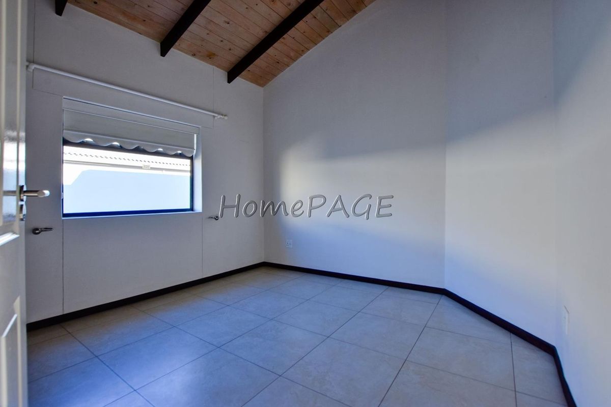A bright, empty bedroom featuring vaulted timber-paneled ceilings, tiled flooring, and a window with a roller blind.