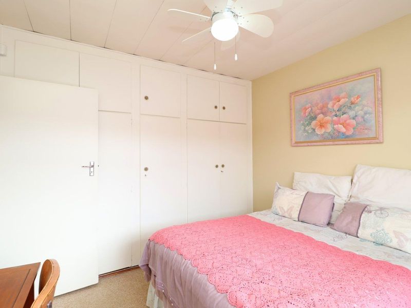 A bedroom featuring built-in cupboards, a ceiling fan, and carpeted flooring.
