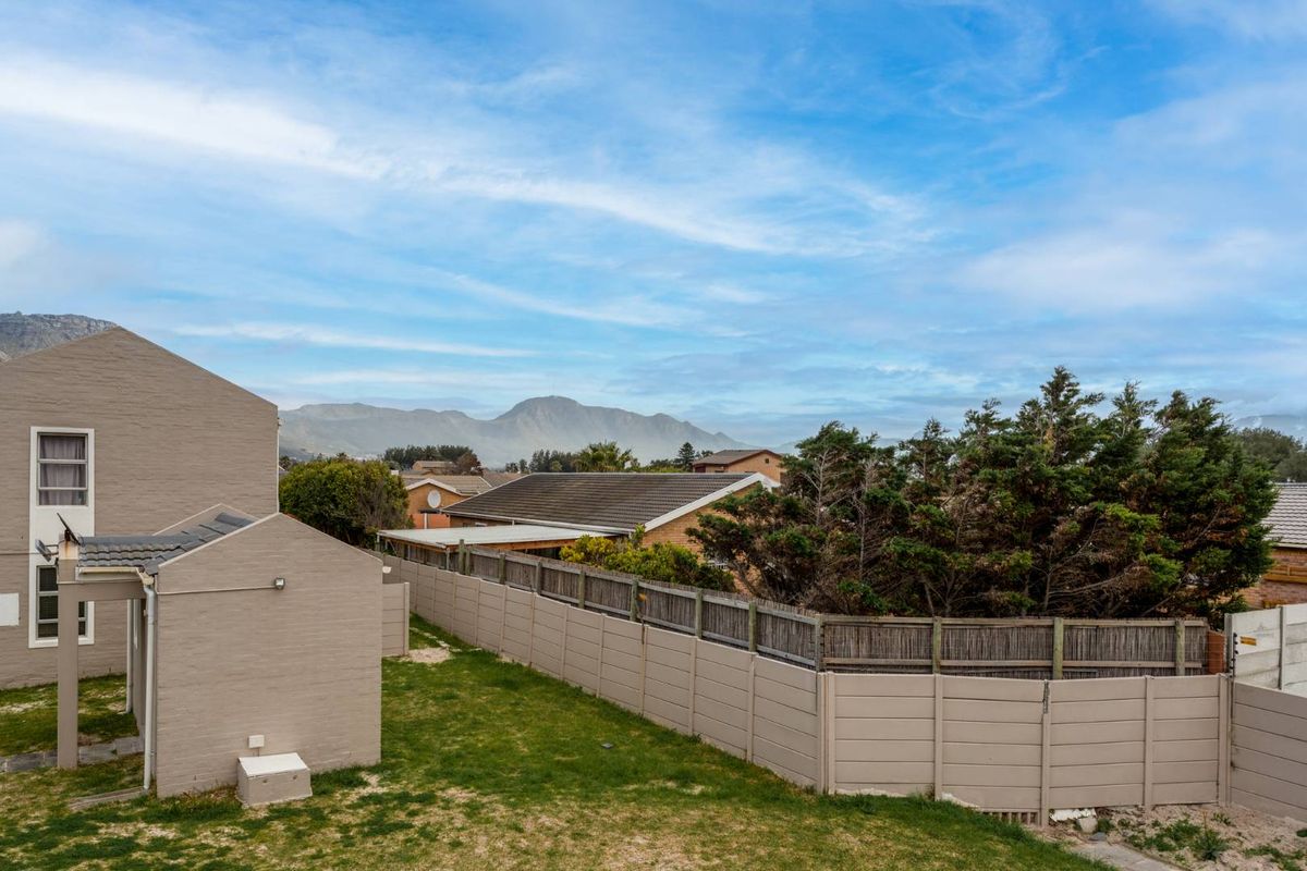 Rear exterior view of the property featuring a lawn area, precast boundary wall, and scenic mountain views in the background.