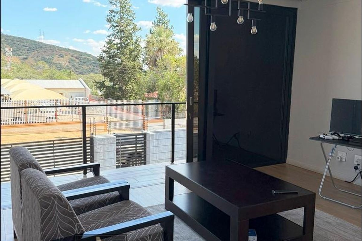 Bright living room featuring modern laminate flooring, recessed lighting, and large sliding glass doors opening onto a balcony with scenic views.