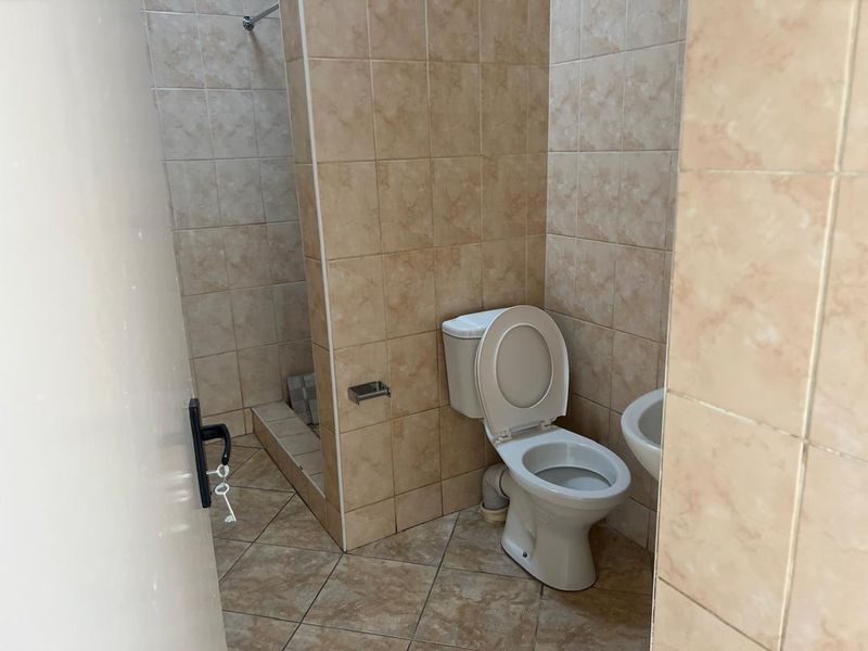 A functional bathroom featuring a toilet, shower area, and washbasin with dated ceramic wall and floor tiling.