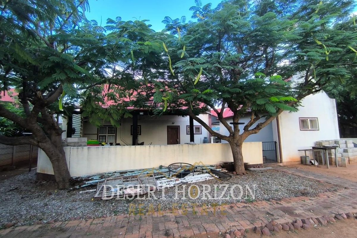 Rear view of the property featuring a covered patio area, mature trees, and a gravel yard space.