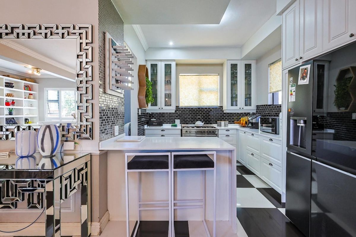 Modern kitchen featuring white cabinetry, black tiled backsplash, stone countertops, and a breakfast bar, seamlessly integrated with the adjacent living area.
