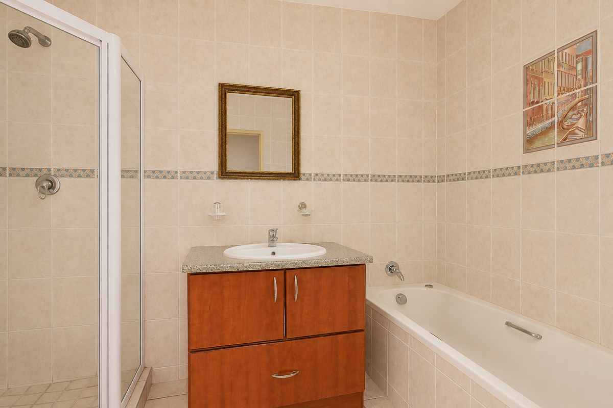 A functional bathroom featuring a shower enclosure, a built-in vanity with basin, and a bathtub, finished with neutral wall tiling.