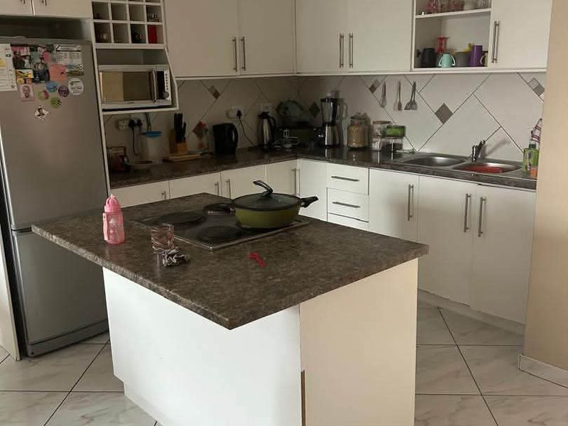 A functional kitchen featuring white cabinetry, laminate countertops, a central island with a built-in hob, and tiled flooring throughout.