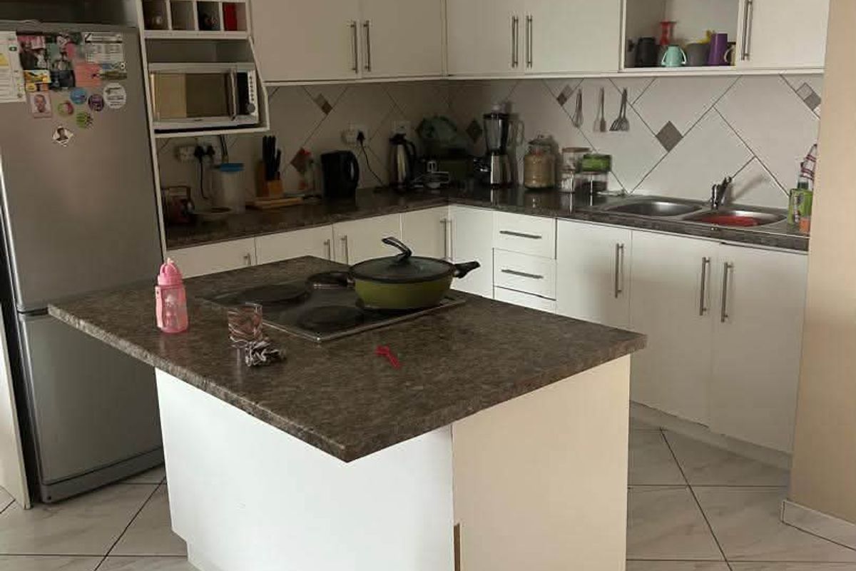 A functional kitchen featuring white cabinetry, laminate countertops, a central island with a built-in hob, and tiled flooring throughout.