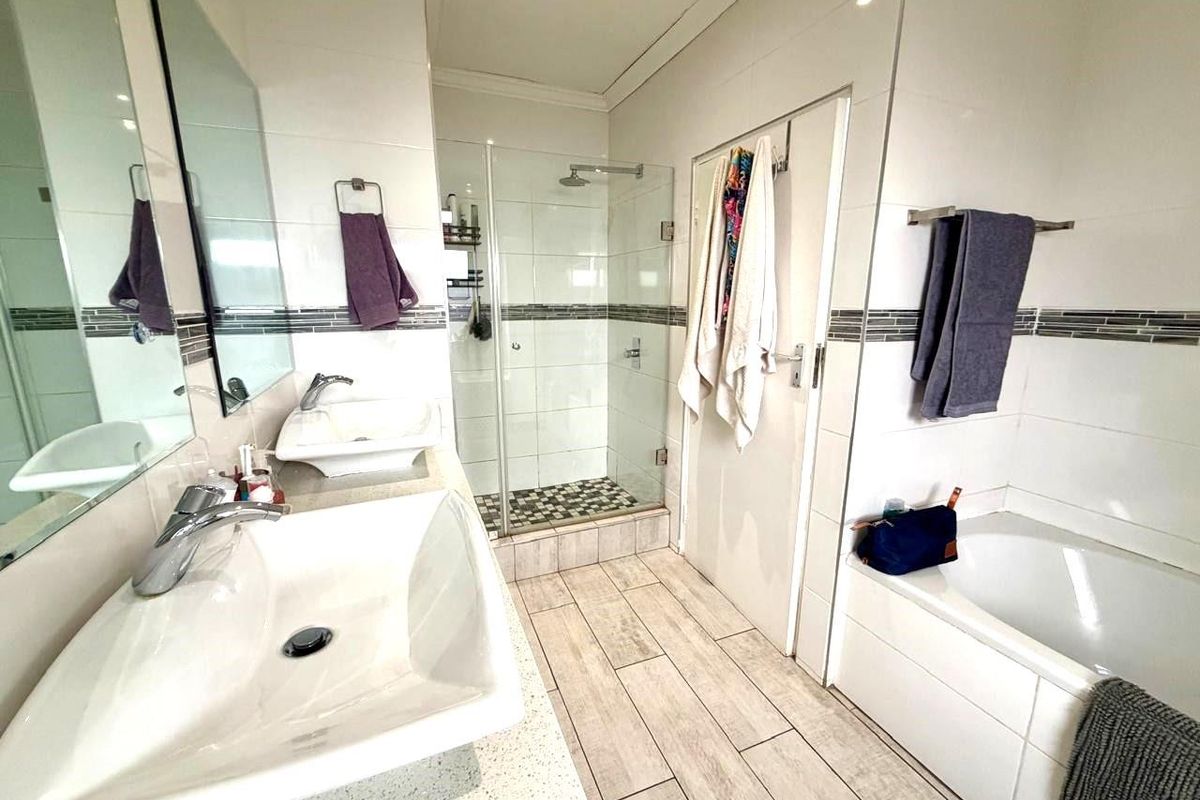 A modern bathroom featuring a double vanity with vessel sinks, a glass-enclosed shower, and a built-in bathtub with tiled finishes.
