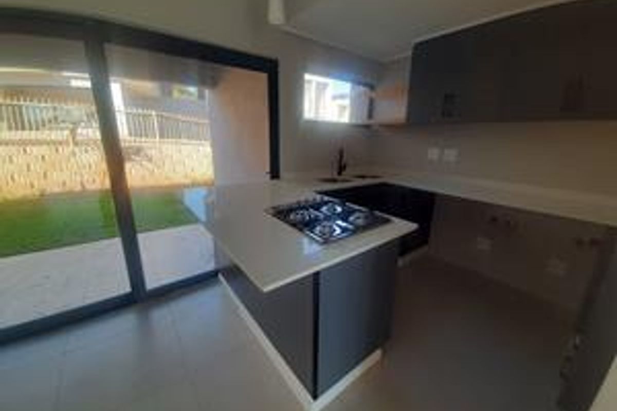 Modern kitchen featuring sleek dark cabinetry, stone countertops, a built-in gas hob, and large sliding doors opening to the garden.