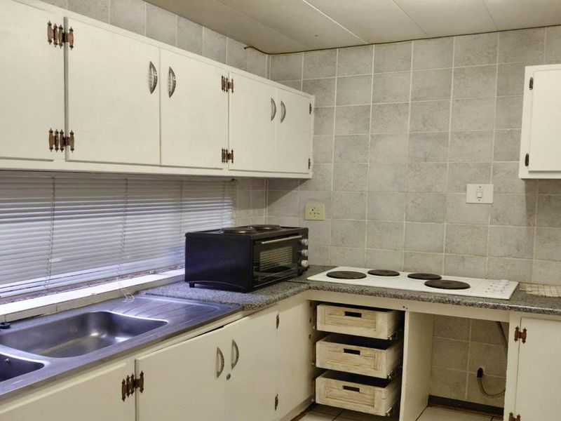 A dated kitchen featuring white cabinetry, a double bowl stainless steel sink, laminate countertops, and a built-in electric hob with tiled backsplash.