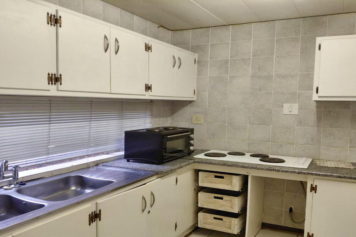 A dated kitchen featuring white cabinetry, a double bowl stainless steel sink, laminate countertops, and a built-in electric hob with tiled backsplash.