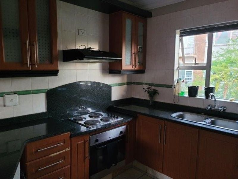 A functional kitchen featuring wooden cabinetry, granite countertops, a built-in oven with hob, and a double sink with a window view.