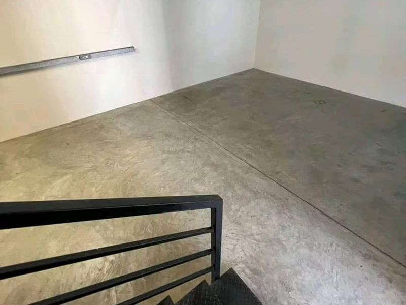An empty garage space featuring concrete flooring and a metal staircase with a black handrail, providing functional storage or parking utility.
