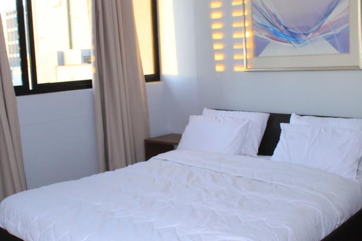 A well-lit bedroom featuring laminate flooring and a large window that allows for natural light.