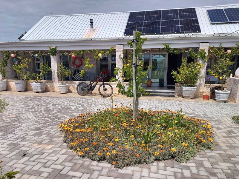 A well-maintained rear exterior featuring a paved courtyard, covered patio with stone pillars, and a roof equipped with solar panels.