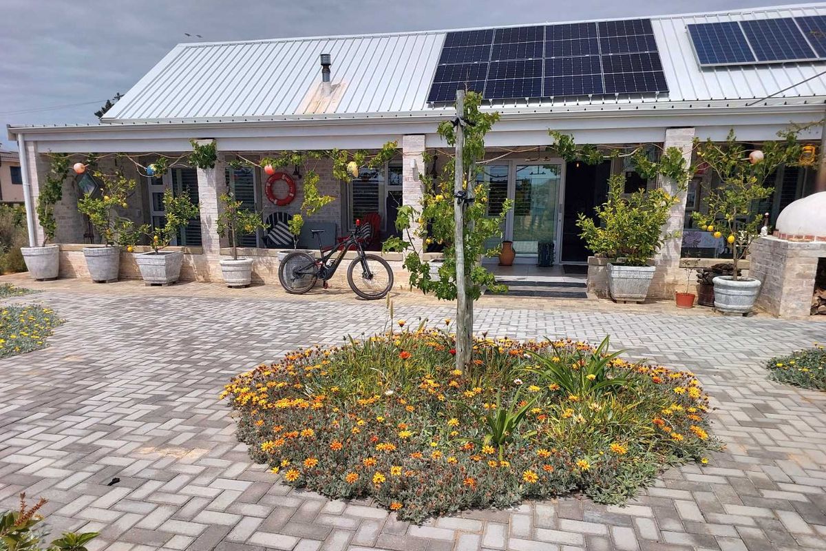 A well-maintained rear exterior featuring a paved courtyard, covered patio with stone pillars, and a roof equipped with solar panels.