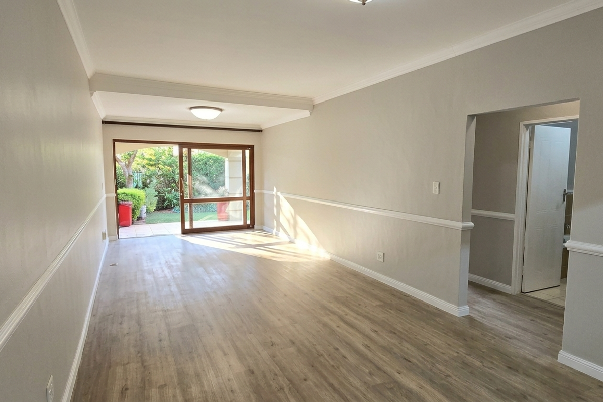 Spacious, light-filled living area featuring modern laminate flooring, elegant chair rail and crown molding, and direct access to a private outdoor patio.
