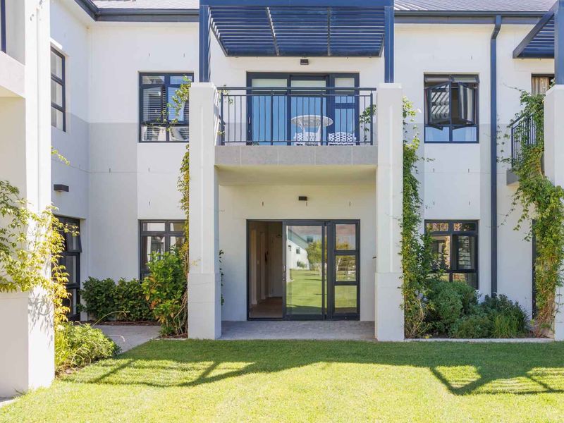 Rear view of the apartment building featuring a ground floor patio, upper balcony with pergola, and well-maintained garden area.