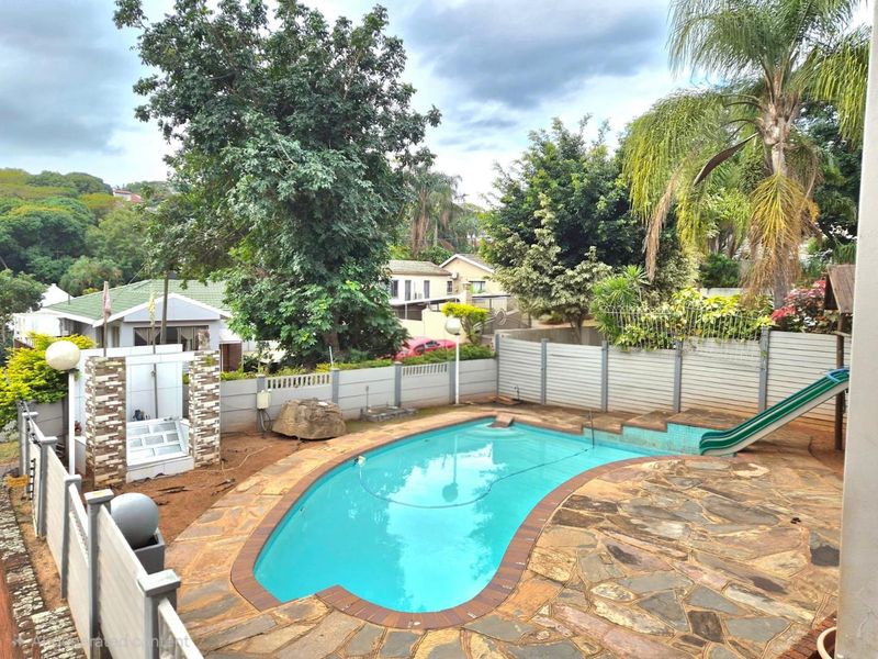 Outdoor pool area featuring stone paving, a built-in shower, and a pool slide, enclosed by boundary walls in a residential garden setting.