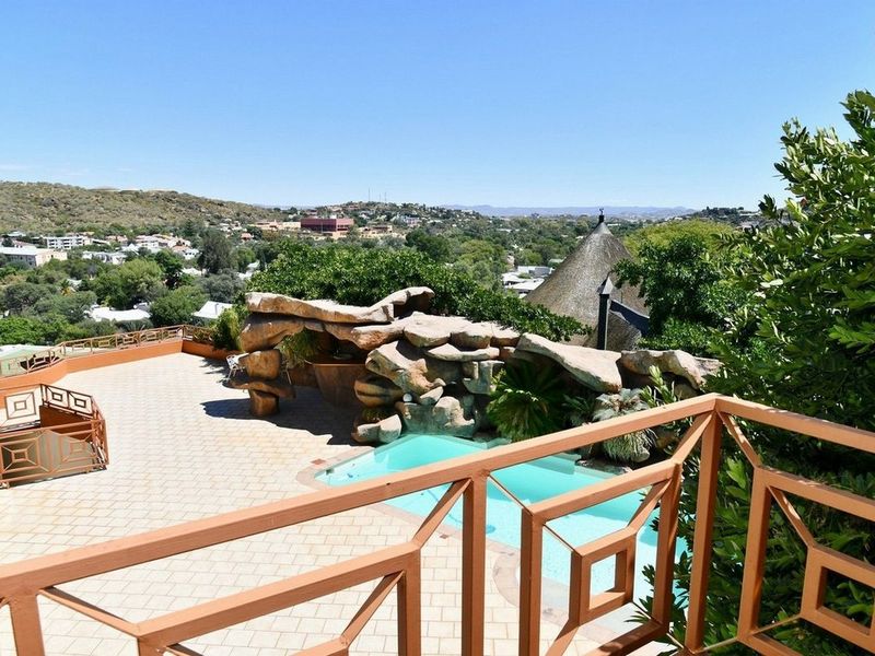 Elevated view of a swimming pool area featuring a decorative rock feature, paved patio, and expansive neighbourhood views.