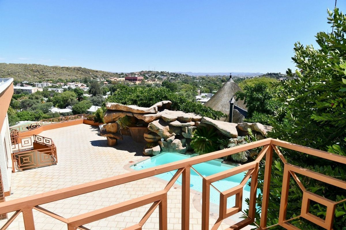 Elevated view of a swimming pool area featuring a decorative rock feature, paved patio, and expansive neighbourhood views.