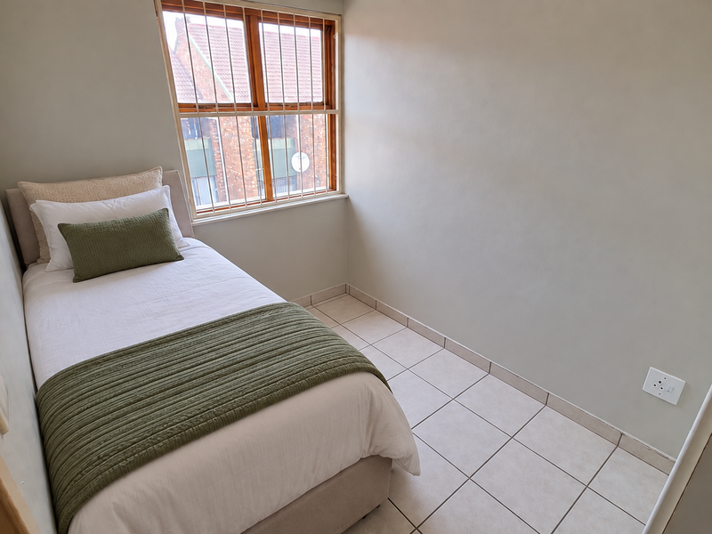 A compact bedroom featuring tiled flooring, a window with security bars, and neutral wall finishes.