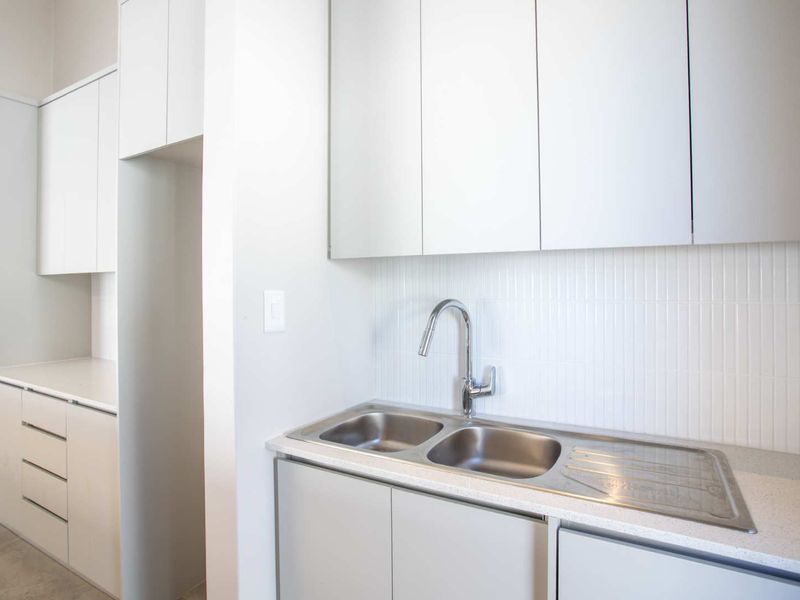 A clean, modern scullery featuring white cabinetry, a double stainless steel sink with a gooseneck tap, and a tiled splashback.