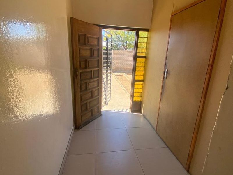 A simple, empty hallway featuring tiled flooring and access to an exterior area through a wooden door.