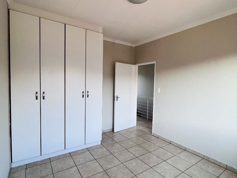 A clean, empty bedroom featuring neutral wall tones, tiled flooring, and ample built-in cupboard storage space.