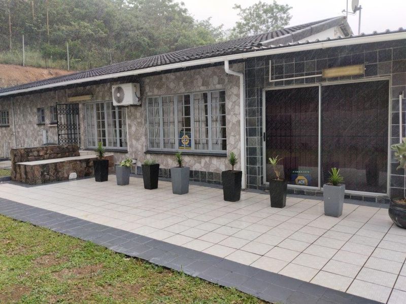 Rear exterior view featuring a tiled patio, stone-clad facade, sliding glass doors with security gates, and an installed air conditioning unit.