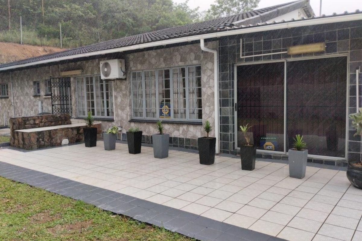 Rear exterior view featuring a tiled patio, stone-clad facade, sliding glass doors with security gates, and an installed air conditioning unit.