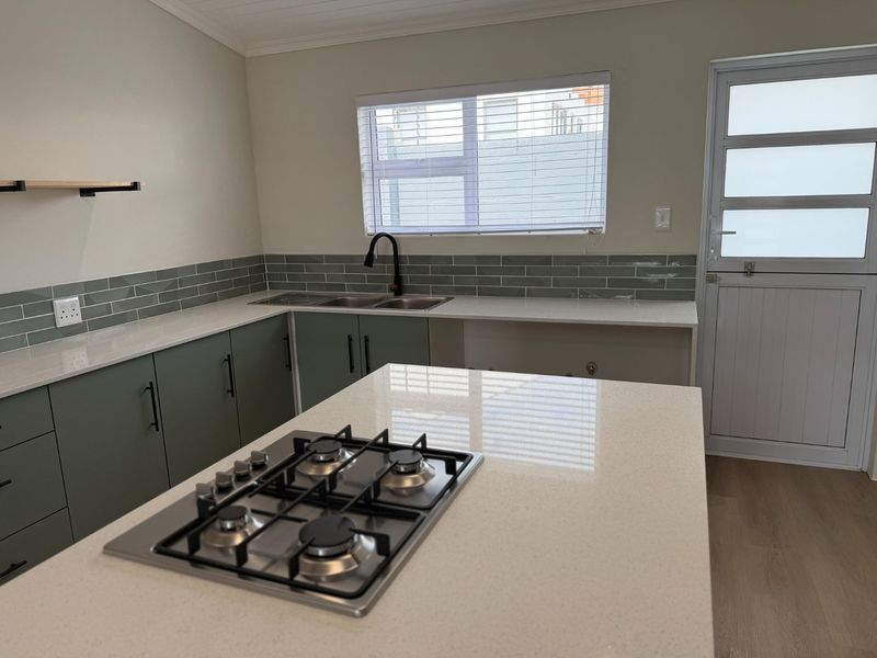 Modern kitchen featuring a central island with a gas hob, stone countertops, subway tile backsplash, and sleek cabinetry.